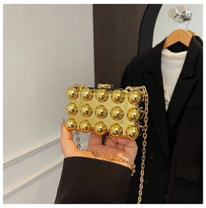 Detail of golden acrylic box clutch featuring hemispherical studs and metal chain strap