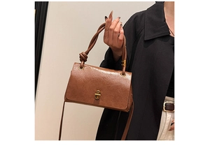 Close-up of retro brown shoulder bag with knotted handle and golden twist lock