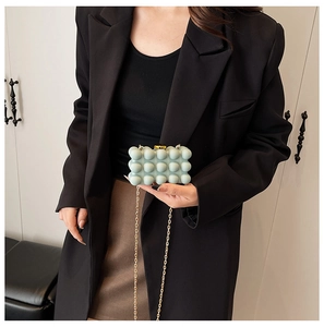 Detail of mint blue acrylic box bag with 3D sphere texture and gold chain worn by model