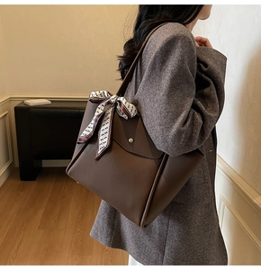 Dettaglio della borsa tote marrone con foulard di seta su una modella in abito grigio