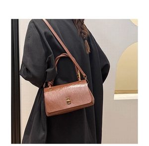 Detailed view of brown glossy leather bag with gold buckle on a black wool coat