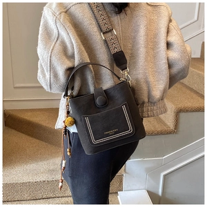 Detail of matte black bucket bag with ethnic woven strap and yellow pompom charm