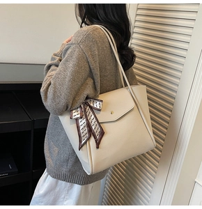 Modella che indossa una borsa tote beige in pelle martellata con foulard decorativo