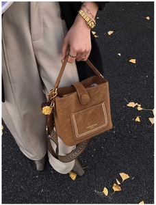 Detail of brown suede bucket bag featuring wide geometric strap and yellow pompom charm