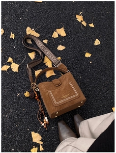 Macro detail of brown suede bucket bag with ethnic embroidery strap and gold rivets