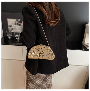 Golden crescent evening bag with metallic mirror finish and delicate chain strap shown on shoulder