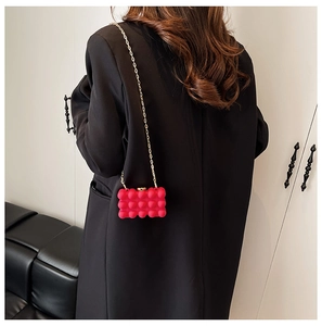 Detail of rose red acrylic box bag with spherical texture and gold chain strap