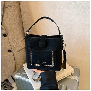 Detail of black pebbled leather bucket bag with gold rivets and woven shoulder strap