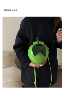Sac à bandoulière en forme de pomme verte en cuir verni brillant sur un manteau en laine