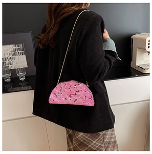 Detail of a bright pink metallic crossbody bag with golden chain on a female model