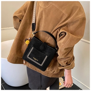 Detail of black crossbody bucket bag featuring geometric strap and yellow pompom