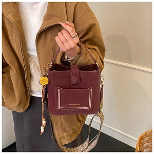 Detail of burgundy bucket bag with wide patterned strap and plush charm accent