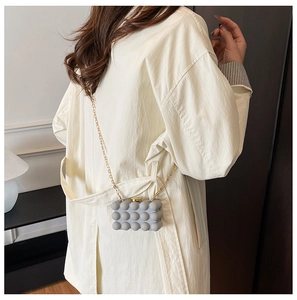 Detail of grey bubble texture clutch bag with golden chain strap on a trench coat