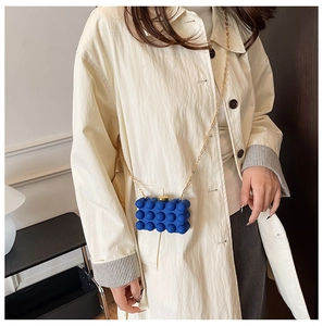 Detail of blue bubble texture acrylic clutch with gold metal chain on a beige coat
