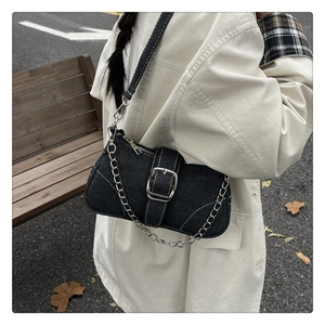 Détail d'un sac à bandoulière en denim noir avec boucle argentée et chaîne en métal