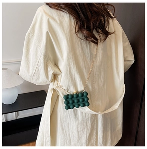 Detail of dark green acrylic clutch featuring bubble texture and gold chain strap