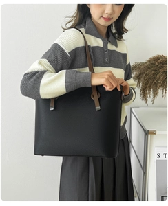 Detail of black pebbled leather tote bag with brown straps worn by a model