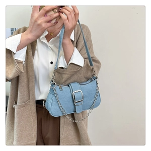 Détail du sac baguette en jean bleu clair avec boucle en métal argenté et chaîne décorative
