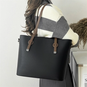 Detail of black tote bag with brown straps and metallic edge trim in lifestyle setting