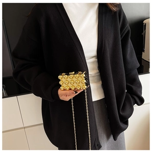 Detail of gold box clutch bag with spherical rivets and metal chain strap on model