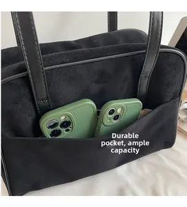 Detail of black suede tote bag showing durable front pocket holding two smartphones