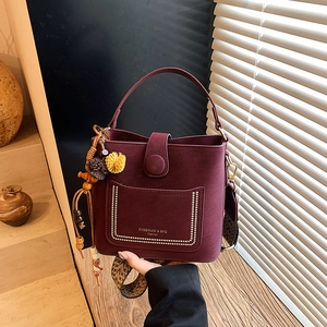Burgundy bucket bag with ethnic woven strap and golden rivet detailing on front