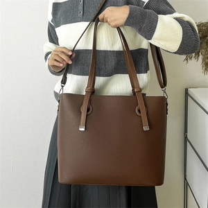 Detail of dark brown tote bag featuring pebbled texture and metal handle reinforcement