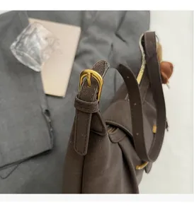 Close-up of matte brown shoulder bag showing gold metal buckle and zipper detail