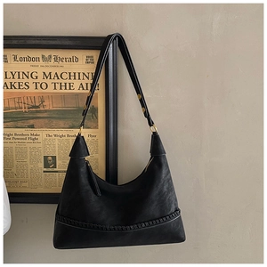 Detail of black leather shoulder bag featuring intricate hand-woven texture and gold buckle