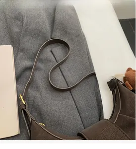 Detail of adjustable strap and plush bear charm on a brown matte leather shoulder bag