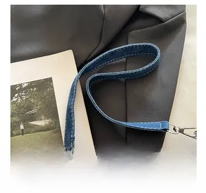 Détail de la bandoulière en denim bleu foncé avec surpiqûres blanches et boucle métallique
