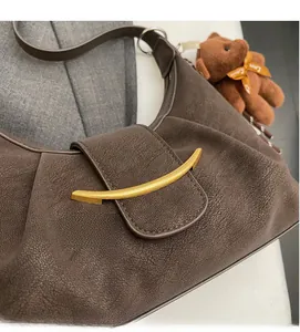 Detail of dark brown crescent bag with gold metal buckle and plush bear charm