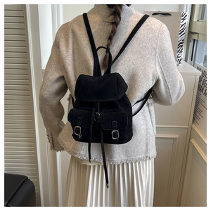 Back view of a black suede mini backpack with silver buckles in a minimalist interior