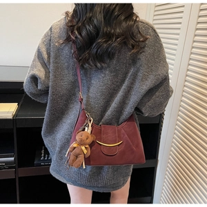 Detail of burgundy half-moon shoulder bag with gold metal buckle and plush bear charm