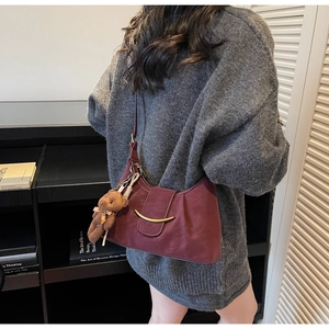 Detail of burgundy leather crescent shoulder bag with gold clasp and plush bear charm
