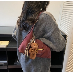 Detail of burgundy leather crossbody bag with golden crescent buckle and teddy bear charm