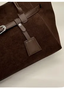 Detailed macro view of dark brown suede tote bag with silver metal buckles and neat stitching