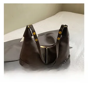 Detail of dark leather bag with woven trim, gold rivets, and zip closure shown on a bed
