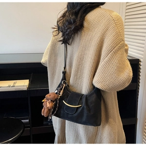 Detail of black leather crescent shoulder bag with golden buckle and plush bear charm