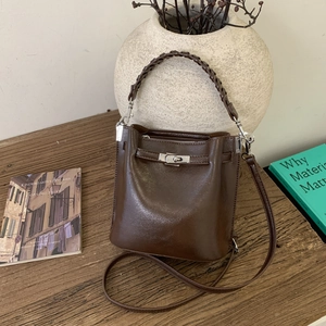 Dunkelbraune Retro-Beuteltasche mit Flechtgriff und Metalldrehverschluss auf Holz