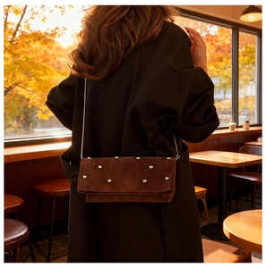 Detail of dark brown suede crossbody bag with silver stud accents and chain strap