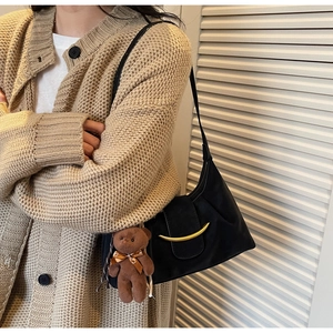 Detail of black underarm bag featuring golden crescent buckle and plush bear pendant