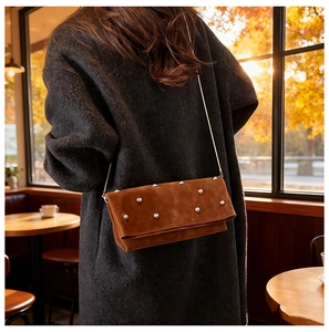Detail view of brown suede crossbody bag with silver rivets and metal chain strap