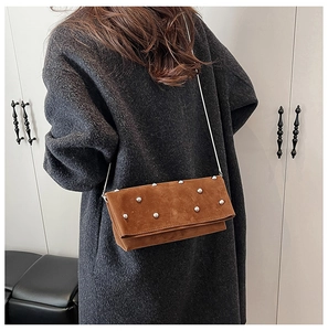 Detail of brown suede crossbody bag with silver studs and fine chain on a grey wool coat