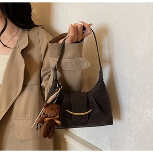 Detail of dark brown leather baguette bag with gold buckle and plush bear charm