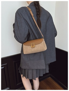 Detail of a brown leather and beige suede shoulder bag with gold rectangular buckle on model