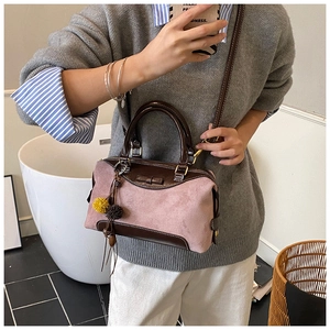 Pink suede crossbody bag with brown leather handles and a colorful pompom charm detail
