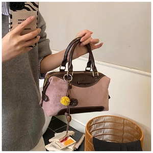 Detail of pink suede Boston bag with brown leather handles and decorative pom-pom charms