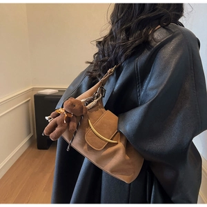 Close-up of brown matte underarm bag with gold moon clasp and teddy bear charm accessory