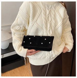 Detail of black suede bag with silver studs and chain strap held by a model in sweater